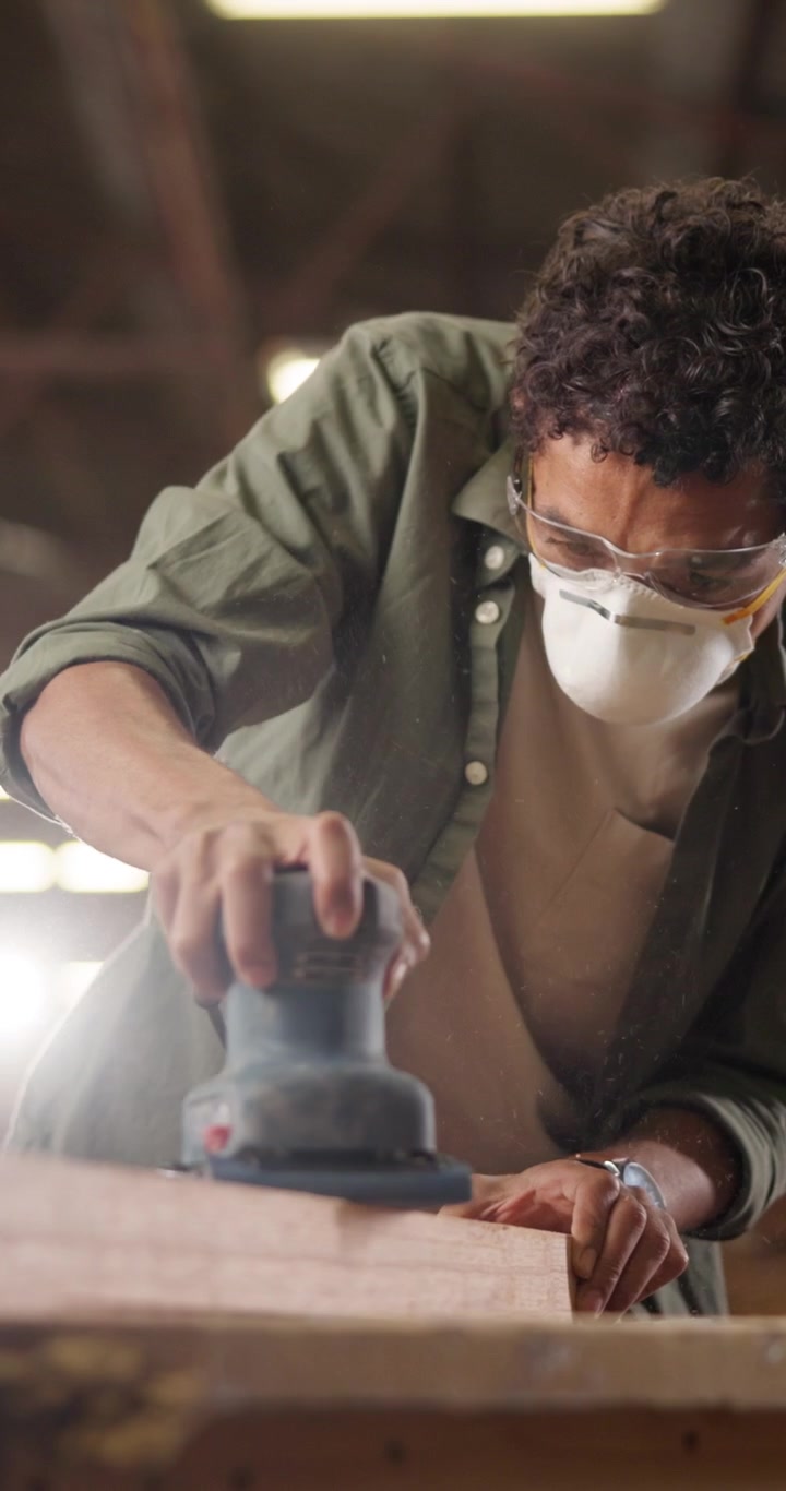 Young Carpenter Sanding Wood Plank in Workshop