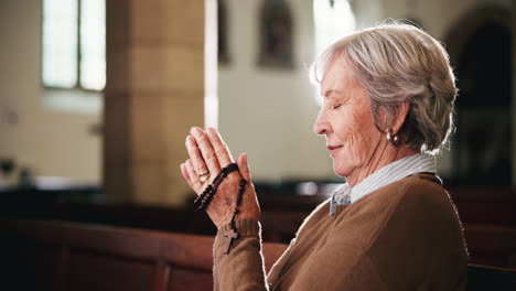 elderly woman praying with rosary in church