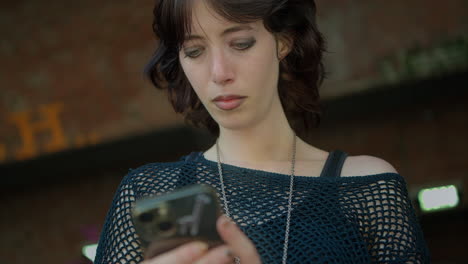 outdoor fashion shot of young alternative style woman using mobile phone on london city street uk in real time