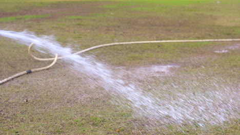 man is spraying water on the cricket ground garden with pipe slow motion