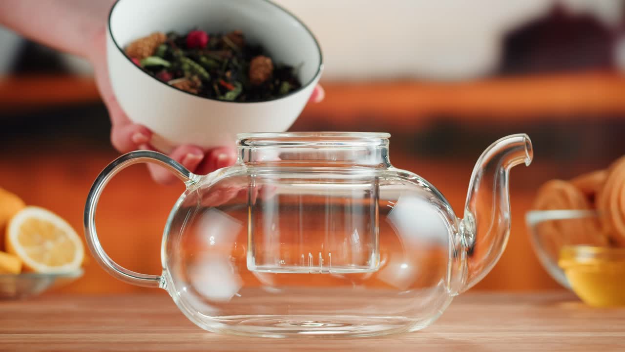 Hand Adding Dry Tea and Ingredients to Glass Teapot for Brewing