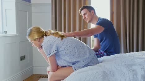 hombre sentado en el extremo de la cama en casa consolando a una mujer que sufre de problemas de salud mental