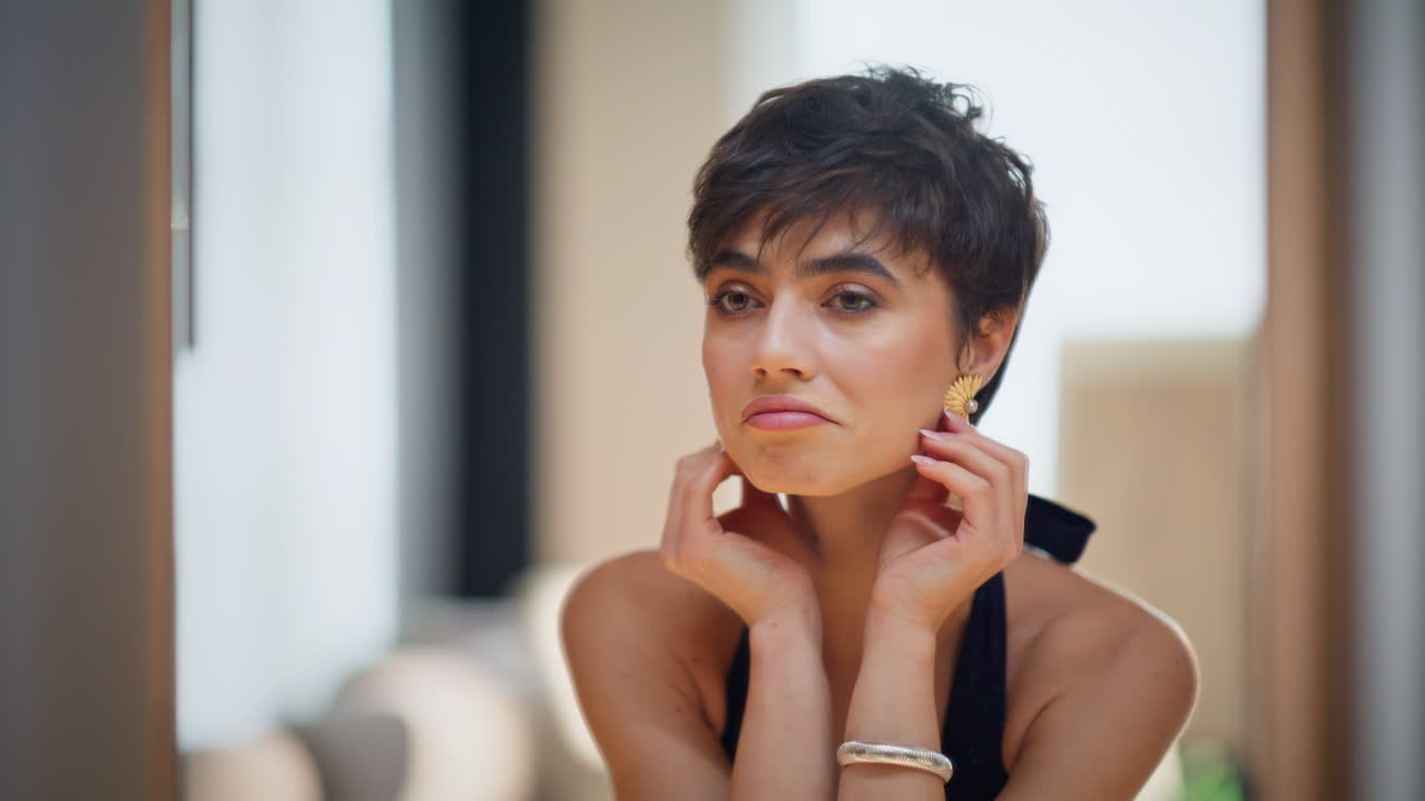 Modella elegante si sistema gli orecchini guardandosi allo specchio e ammirando il suo riflesso, primo piano.
