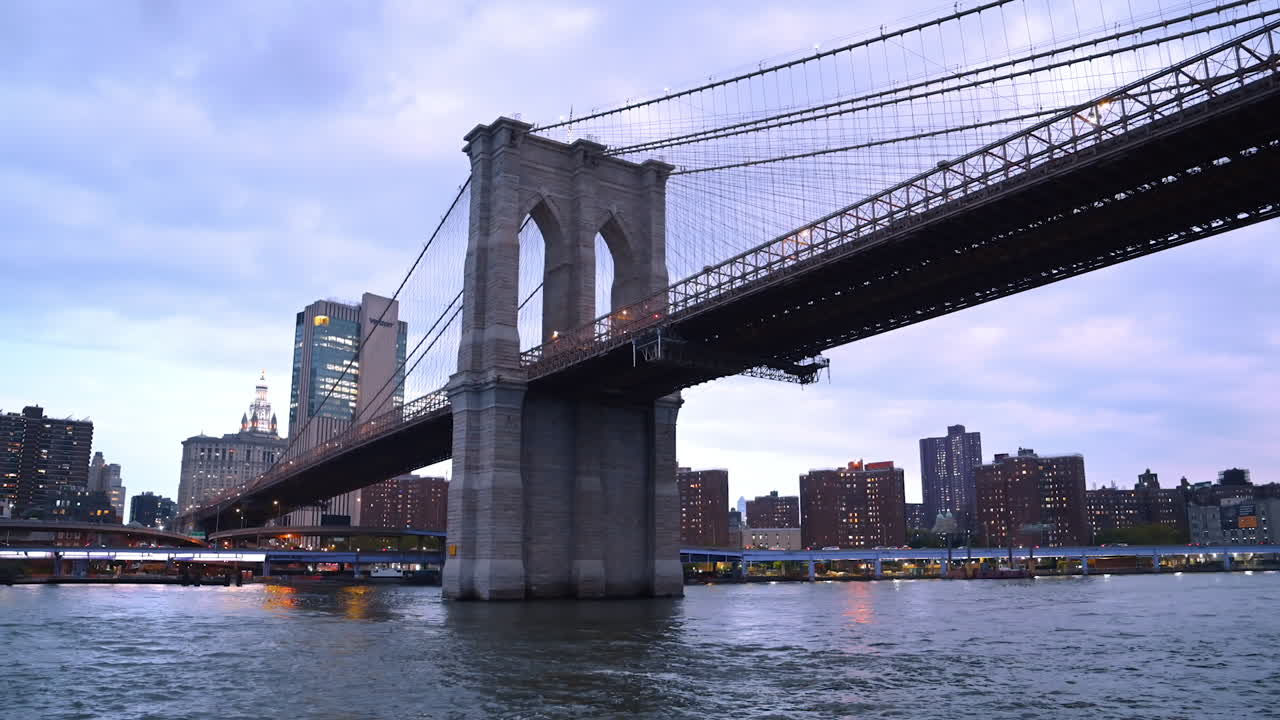 New York, USA, 1 August 2025: Brooklyn Bridge across the East River at dusk. The Brooklyn Bridge stretches over the East River with evening city lights in the background
