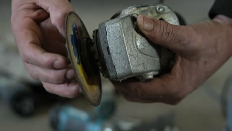 primer plano de las manos de un trabajador quitando el disco abrasivo de una amoladora angular para cambiar