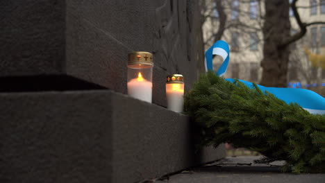 Shot-of-a-couple-of-candles-burning-and-a-green-Christmas-reef-lying-next-to-a-stone-plaque,-Christmas-Day