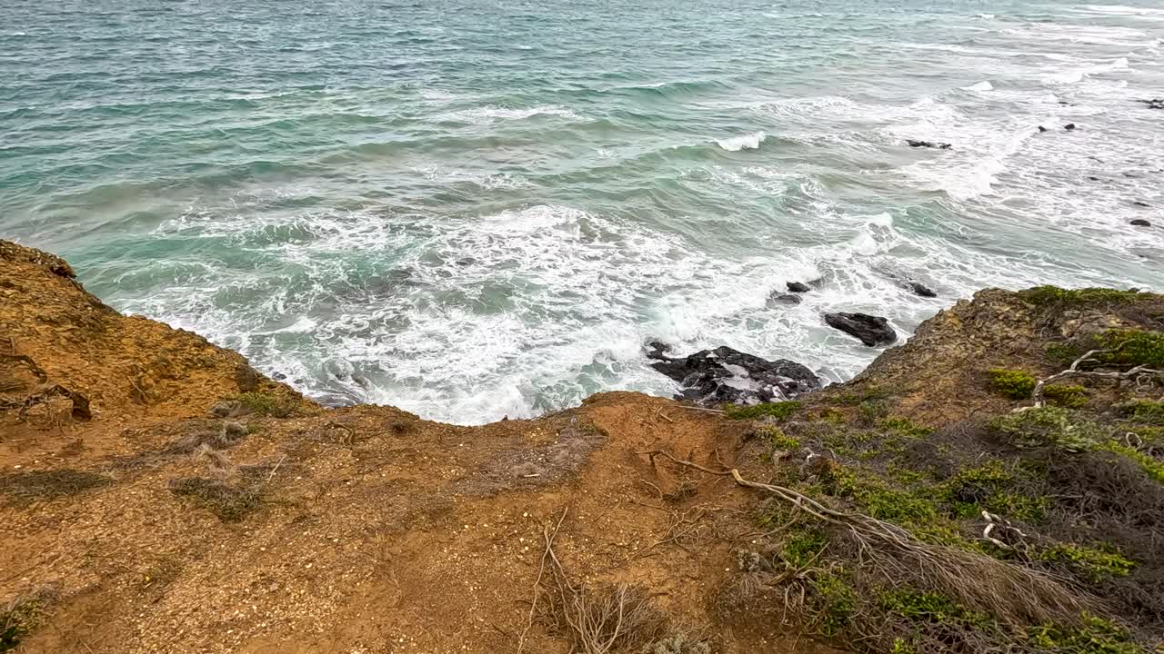 Aerial view of ocean waves hitting rocky cliffs under natural daylight, showcasing dynamic coastal scenery