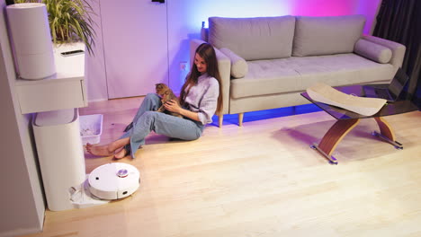 mujer con gato interactuando con vacío robótico en la sala de estar