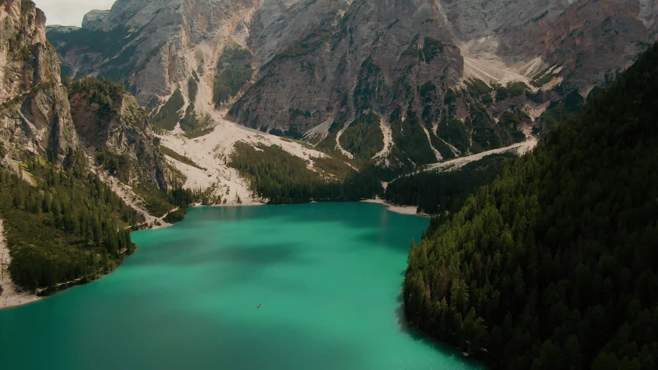 Ripresa con drone in tilt-reveal su un lago di montagna turchese verso le alte montagne sullo sfondo in una giornata di sole.
