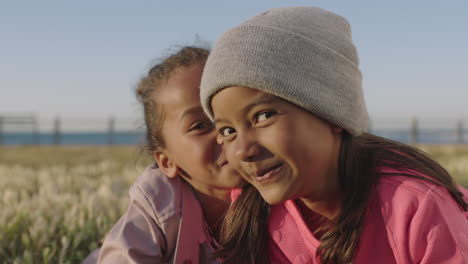 close up portrait of little girls smiling happy playful gossip looking at camera enjoying seaside park together