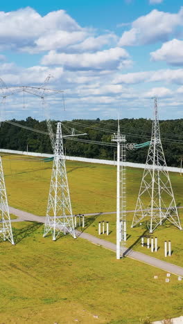 high voltage steel pylons on green field. power transmission lines at sunlight. white electricity towers in summer day. vertical video