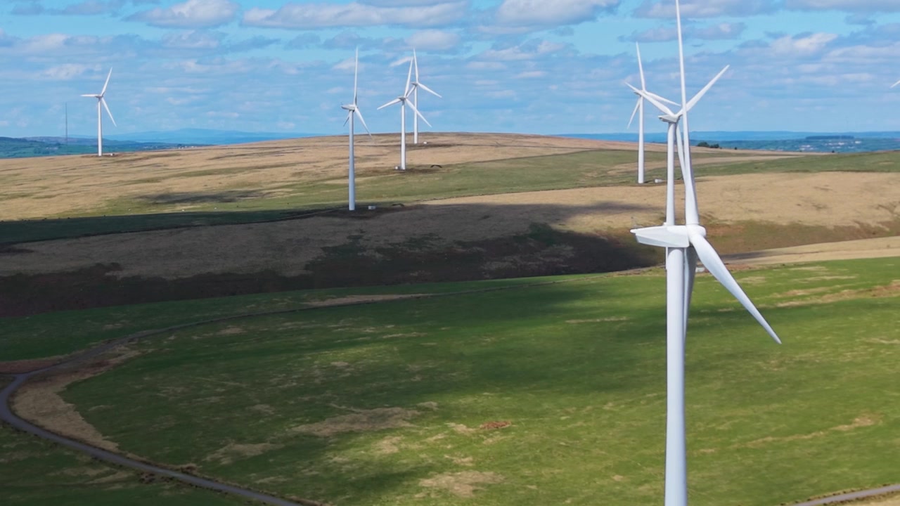 Wind Turbines Spread Across Rolling Hills During Daytime with Close Details of Blades Rotating. Drone Clip of Renewable Energy Generation Infrastructure in UK. 4K.