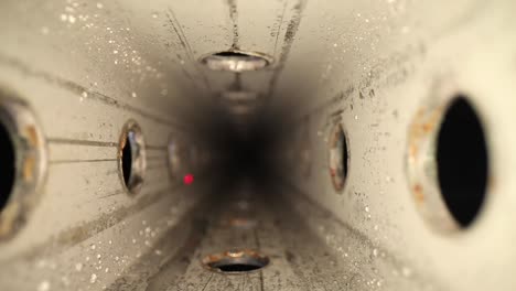 slowly pulling out of a wet zinc-plated steel perforated square tube with a wide angle macro probe lens - as a red laser light darts around inside the tube, through the side holes