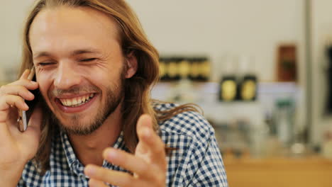 Close-up-view-of-caucasian-blond-man-with-long-hair-talking-on-the-phone-sitting-at-a-table-in-a-cafe