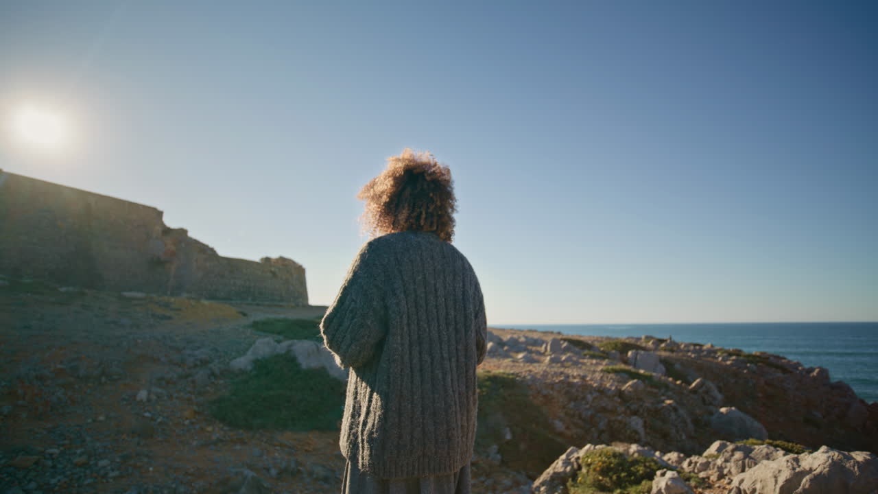 Travel girl crossing hills exploring marine nature back view. Curly lady walking