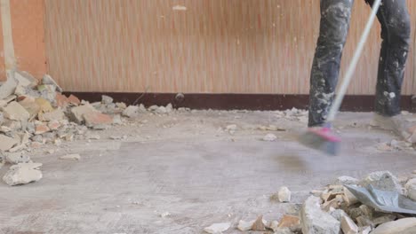 worker cleaning debris with broomstick on a renovation indoor with dust everywhere