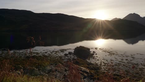 Ein-Goldener-Sonnenstrahl-Wird-Von-Der-Flachen-Oberfläche-Eines-Gezeitensees-Im-Nordwestlichen-Schottischen-Hochland-Reflektiert,-Kurz-Bevor-Er-Hinter-Der-Silhouette-Eines-Berges-Untergeht