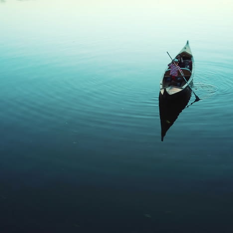 woman and a gondolier floating in a boat on the evening river. man in white hat and striped shirt carring elegant woman with lantern in a boat. quick aerial view around.
