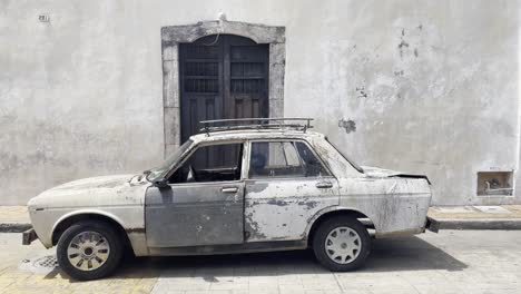 Altes-Verwittertes,-Verrostetes,-Klassisches-Weißes-Auto-Mit-Gestellen-An-Einer-Flachen-Grauen-Gebäudewand-In-Valladolid,-Mexiko