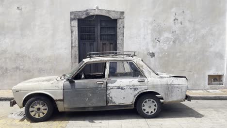 old weathered rusted classic white car with racks against flat grey building wall in valladolid mexico