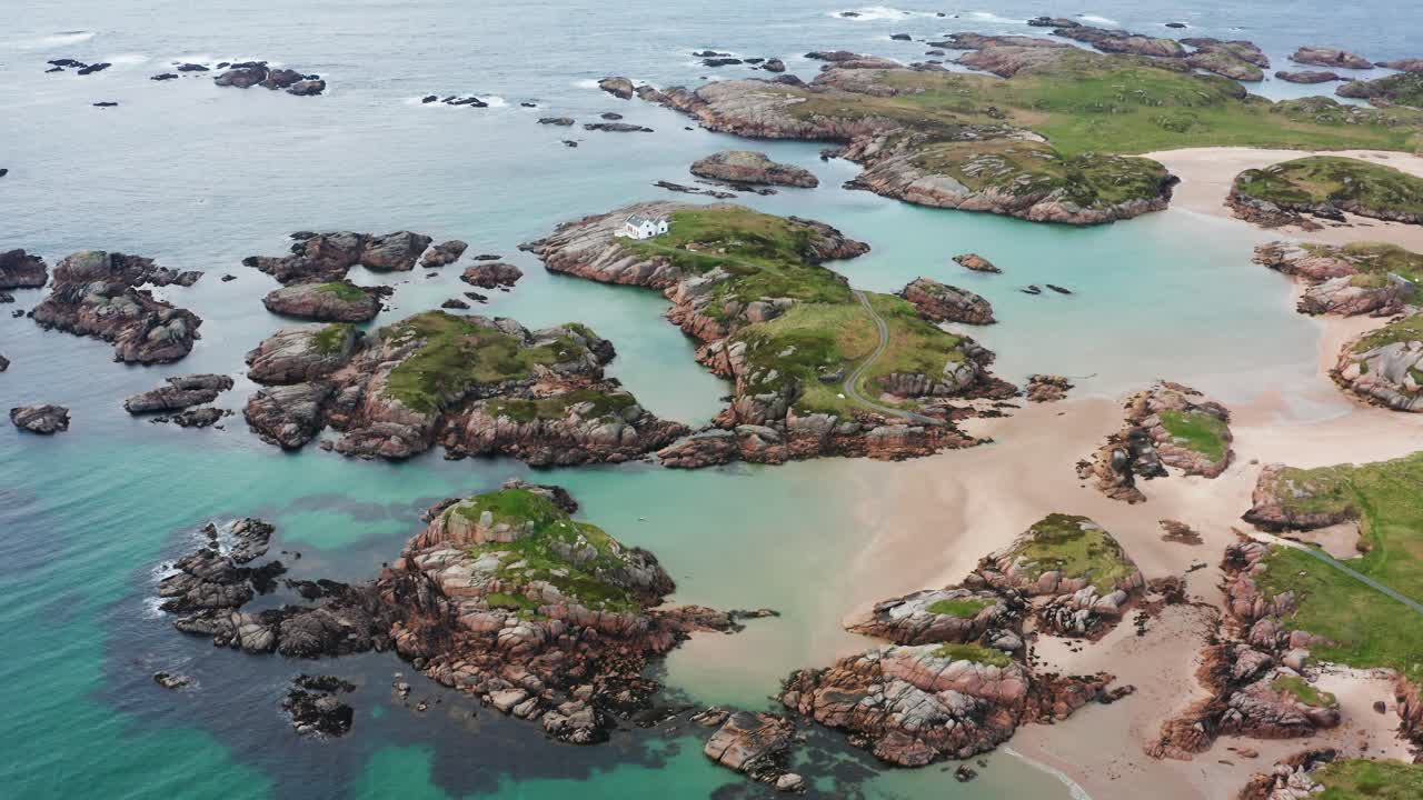Aerial View of Cloughglass Bay’s Stunning Grass Covered Rocky Outcrops and a White House on the Irish Coastline