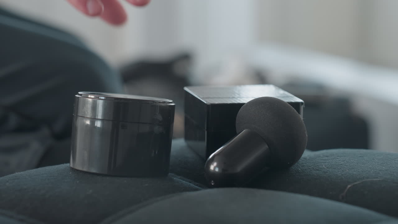 close up of fair skinned man hand collecting black makeup container and box from cushioned seat leaving foam applicator behind, minimalist studio with soft natural light