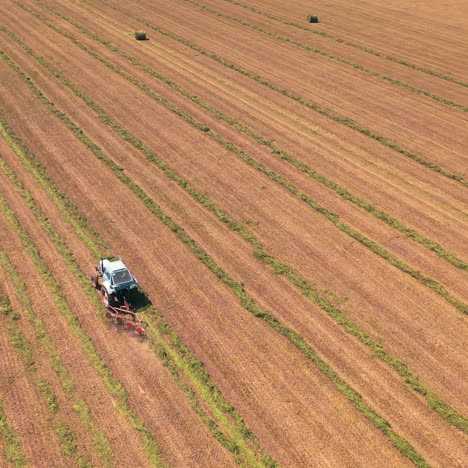 aerial panoramic view of a huge field with agricultural works. tractor scatters grass in a sunny summer day. camera moves bottom up.
