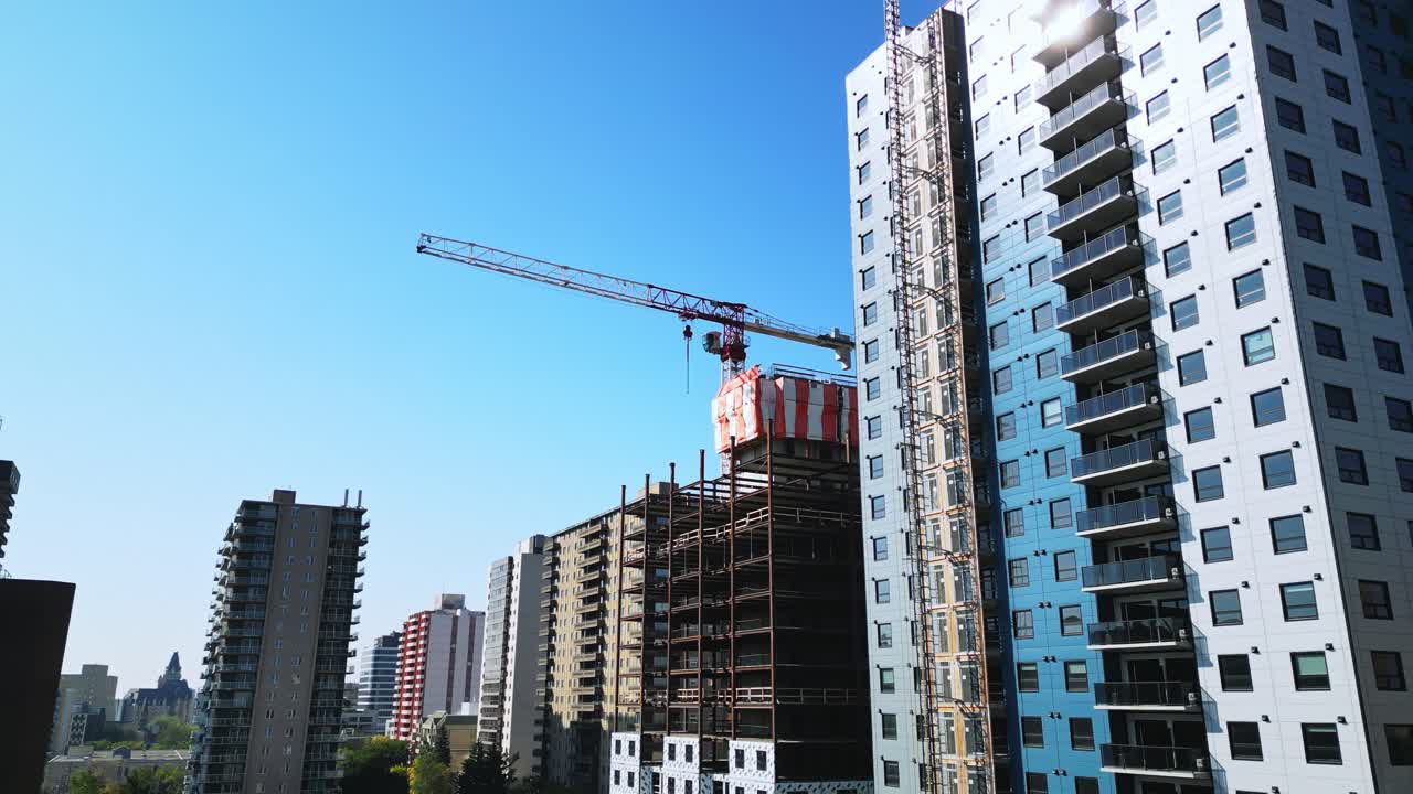 Slow aerial view of large crane above building under construction, blue sky