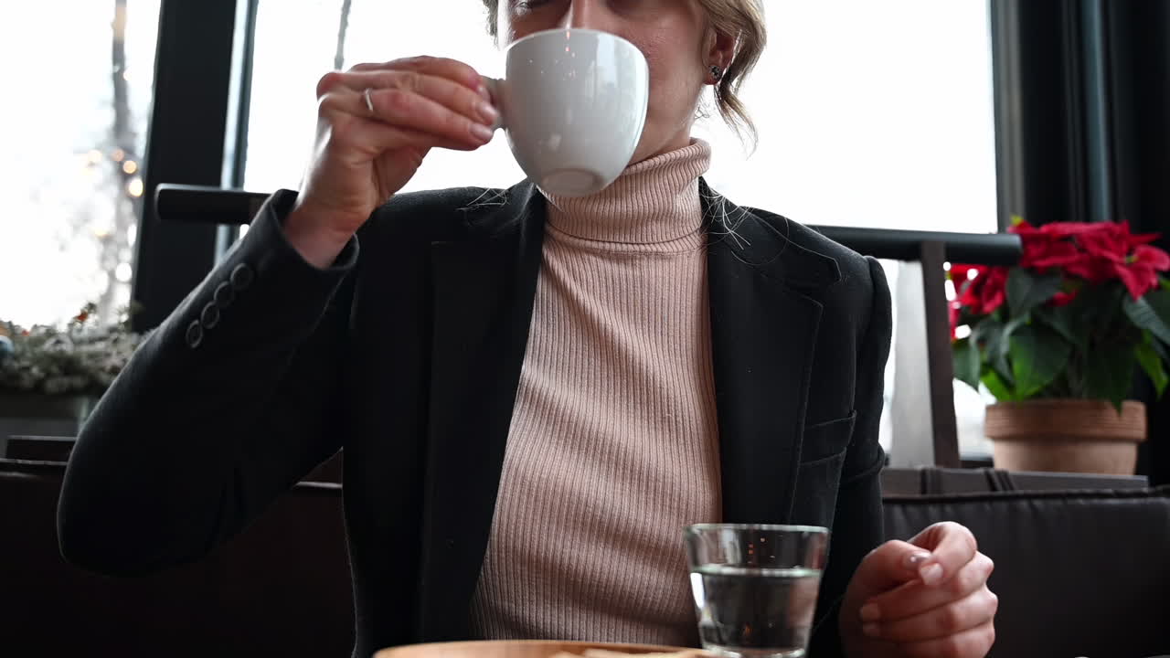 Close up of a woman drinking an espresso with biscotti near a glass of water at a cafe