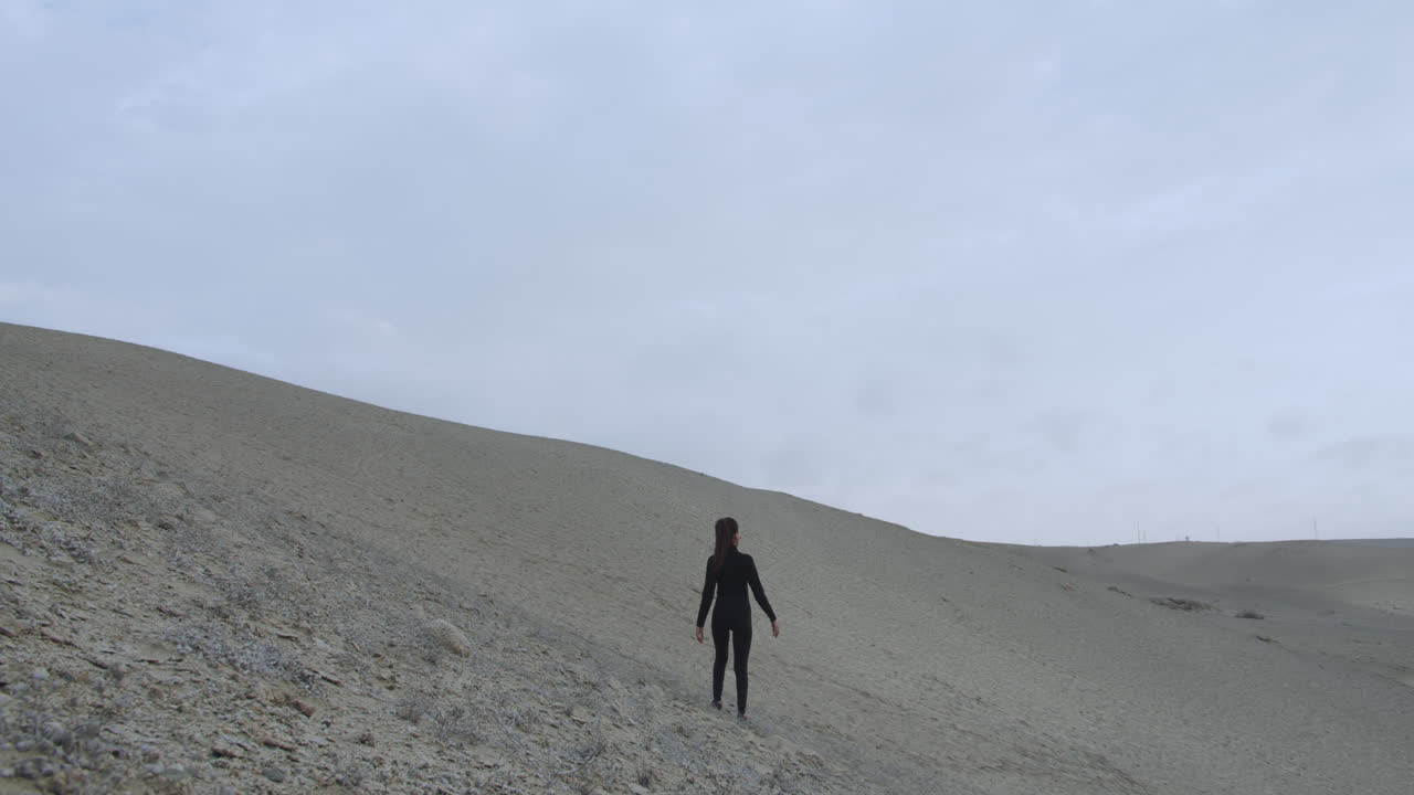 바람이 세차게 부는 사막 한가운데 검은 옷을 입은 여자의 긴 사진