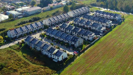 Overhead-aerial-view-of-colorful-autumn-trees,-residential-houses-and-yards-with-drainage-pond-along-suburban-street