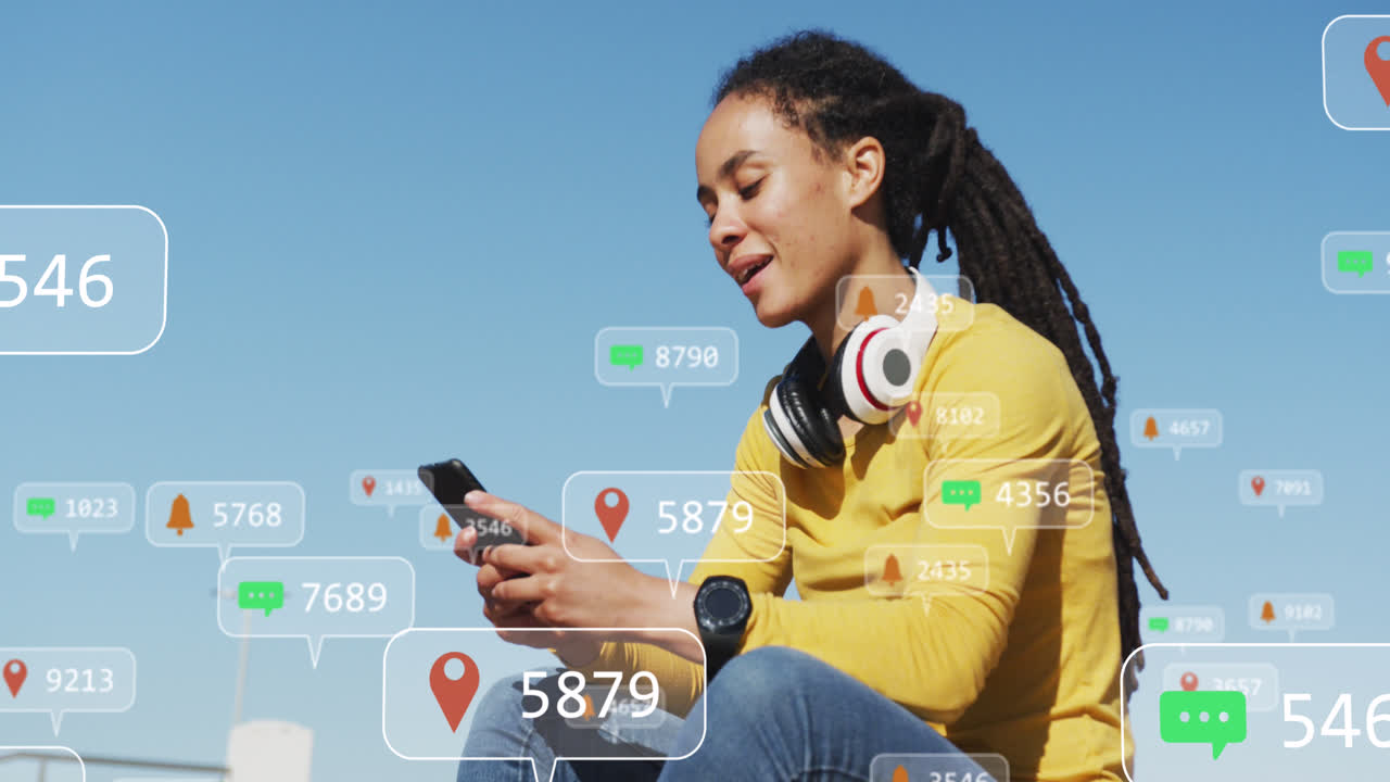 múltiples burbujas de habla con iconos digitales contra la mujer afroamericana que usa un teléfono inteligente al aire libre
