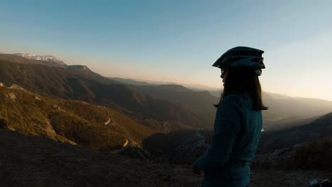 Niña-De-Pie-Con-Su-Bicicleta-En-La-Cima-De-Una-Montaña-Al-Atardecer