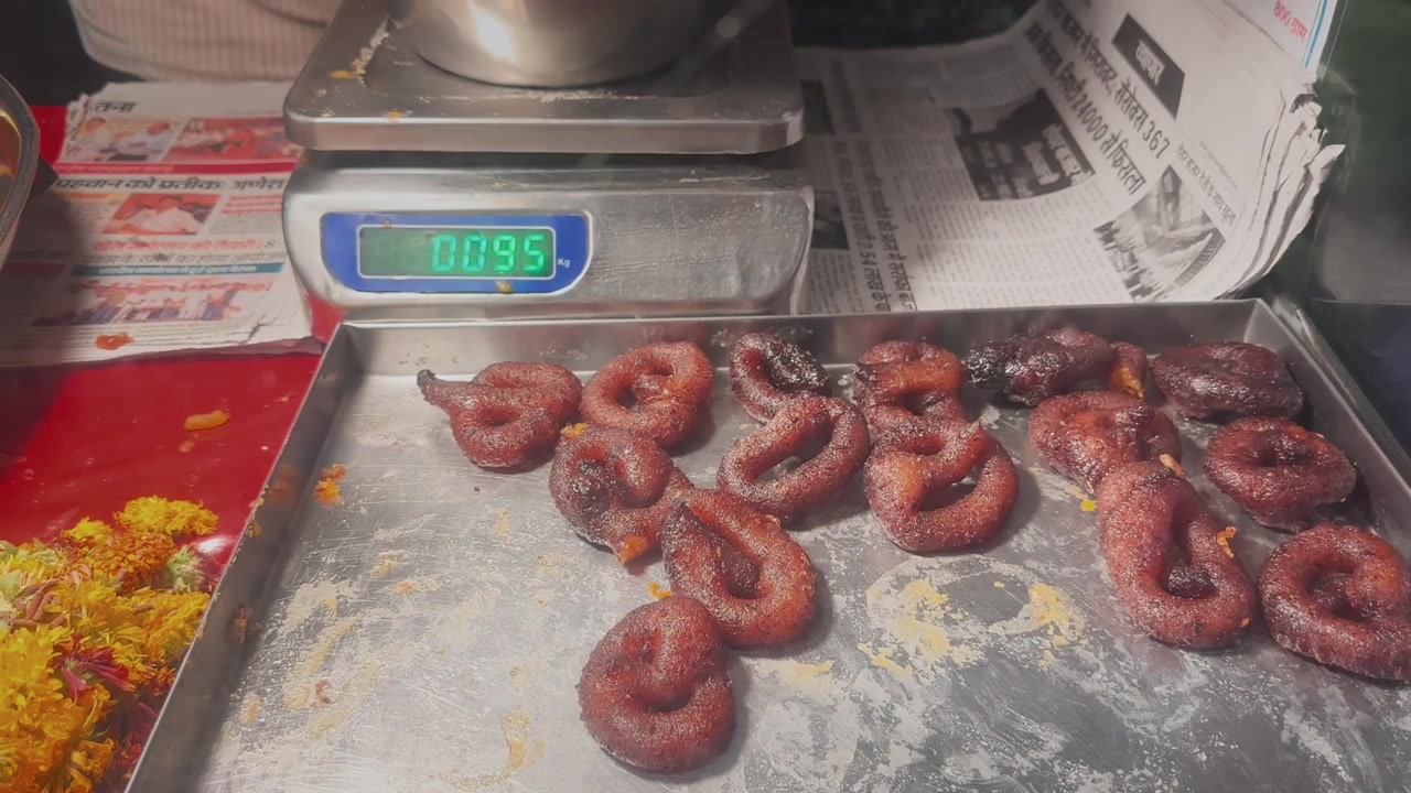 Close-up de um vendedor ambulante servindo mawa jalebi recém-preparado de uma bandeja de metal em uma barraca de doces indiana local.