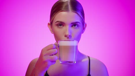 portrait young woman drinking coffee and licking foam off lips, studio shot