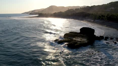 Aerial-shot-of-waves-break-on-rocks-in-a-blue-ocean