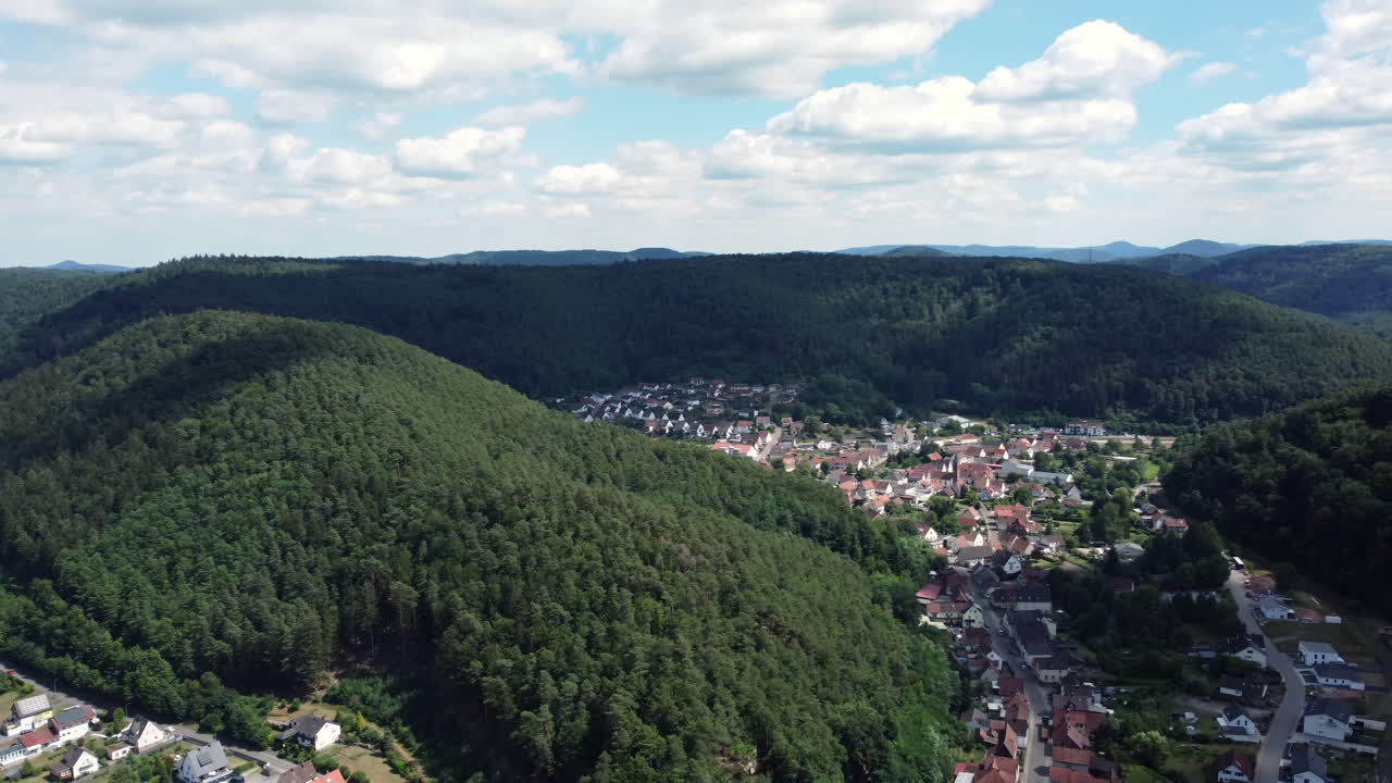 vista aérea de una aldea ubicada en un valle rodeado de montañas y bosques