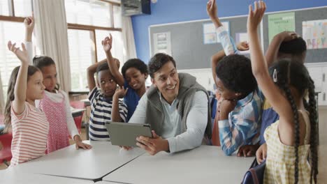 maestro masculino diverso con tableta y niños levantando las manos en la clase de escuela primaria, cámara lenta