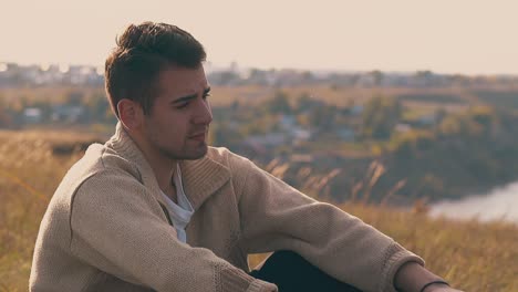 handsome-lonely-guy-sits-on-river-bank-in-autumn-close-slow