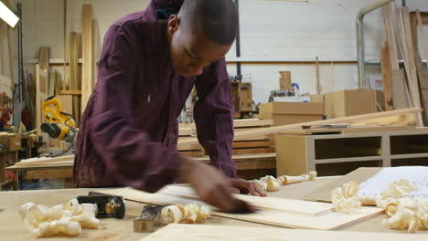 male apprentice sanding wood in carpentry workshop