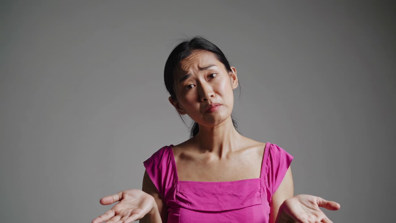 A video still shows a woman in a pink top shrugging, captured from a front-facing angle