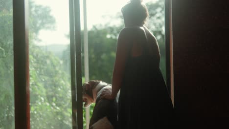 una mujer y yo su perro de pie junto a una puerta abierta, mirando hacia afuera en la vegetación, disfrutando de un momento de paz juntos