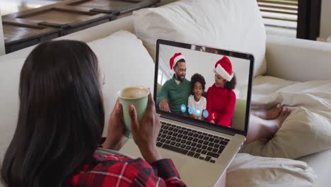 Mixed-race-woman-using-laptop-on-video-chat-with-family-during-christmas-at-home