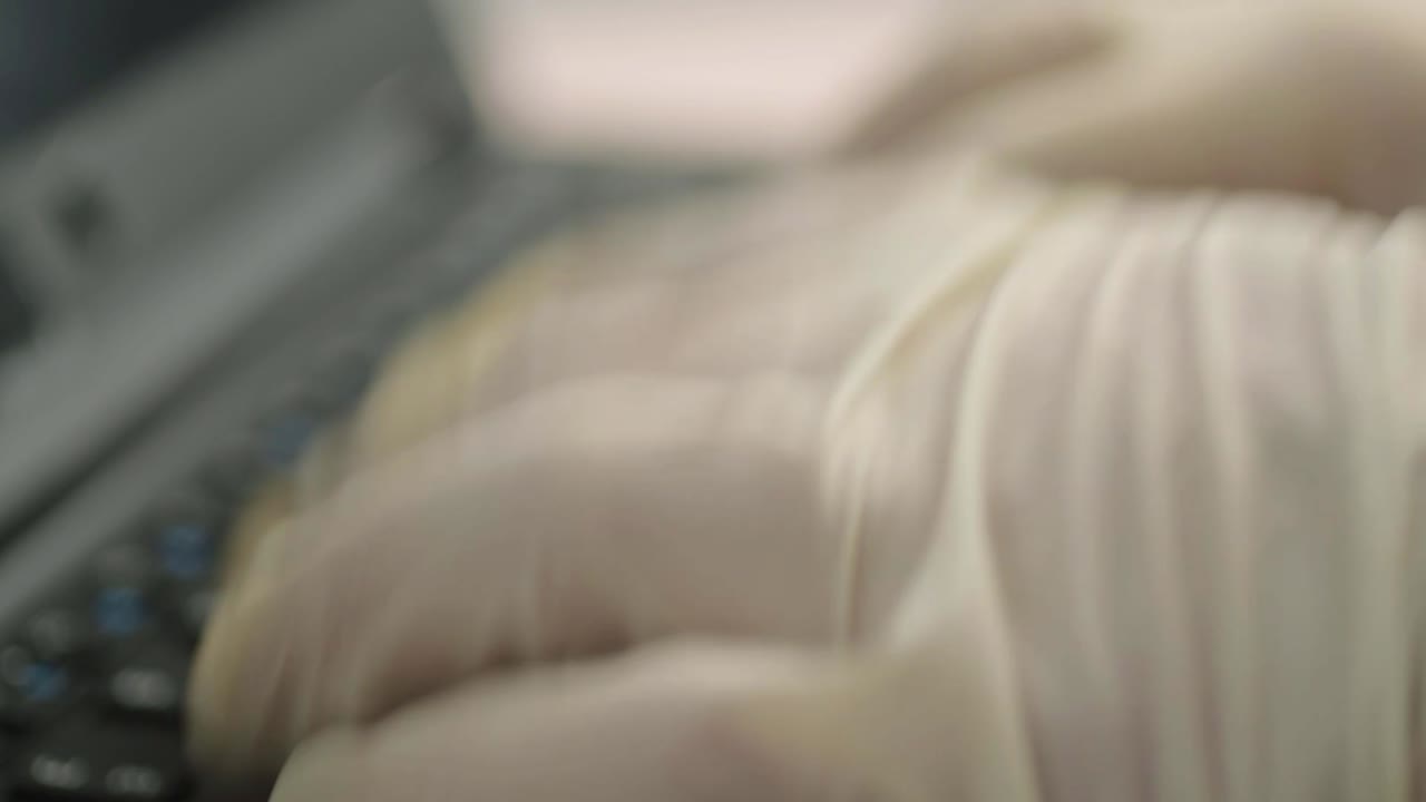 Hand wearing hygienic gloves typing on laptop keyboard close up