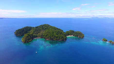aerial footage flies in towards a remote island surrounded by blue ocean water on a calm day at sea in panama