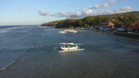 low fly drone to capture traditional balinese sailing fisherman boat in summer on windy evening. amazing colorful sunset and indian ocean with white sand beach and jungle in background