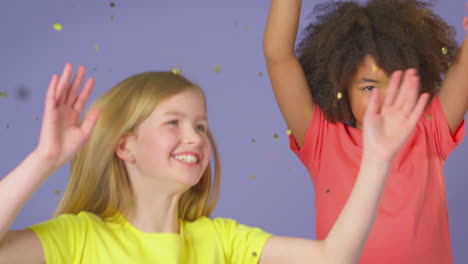 studio shot of children with glitter jumping in the air with outstretched arms on purple background