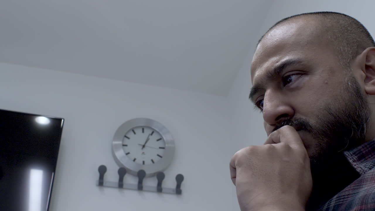 lectura masculina de minorías étnicas con los ojos, la mano en la barbilla en la sala de reuniones con reloj de pared en segundo plano