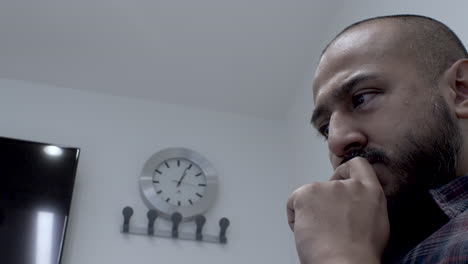 Ethnic-Minority-Male-Reading-With-Eyes,-Hand-On-Chin-In-Meeting-Room-With-Wall-Clock-In-Background