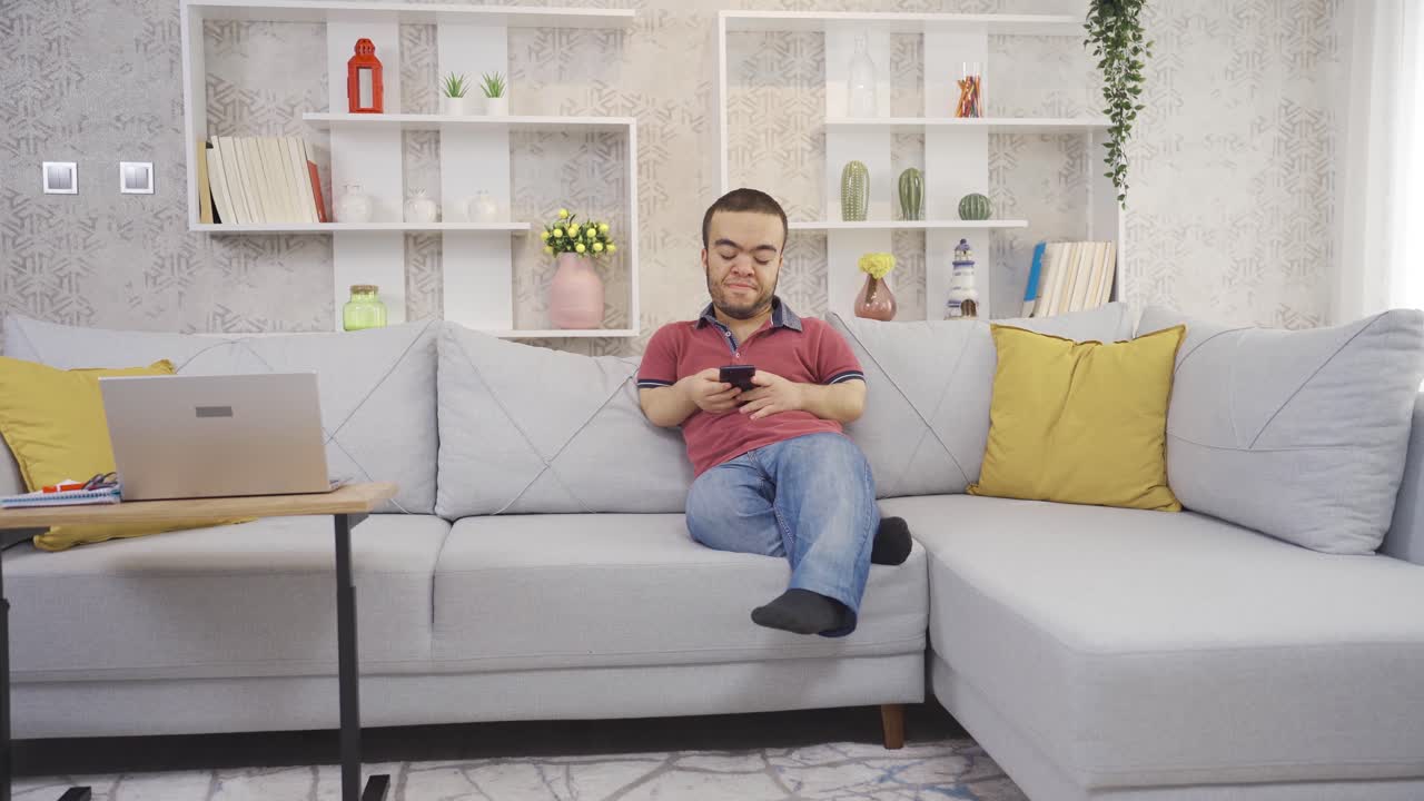 집에 있는 긍정적인 장애인 난쟁이 젊은이가 행복하게 전화를 보고 미소 짓고 휴식을 취하고 있습니다.